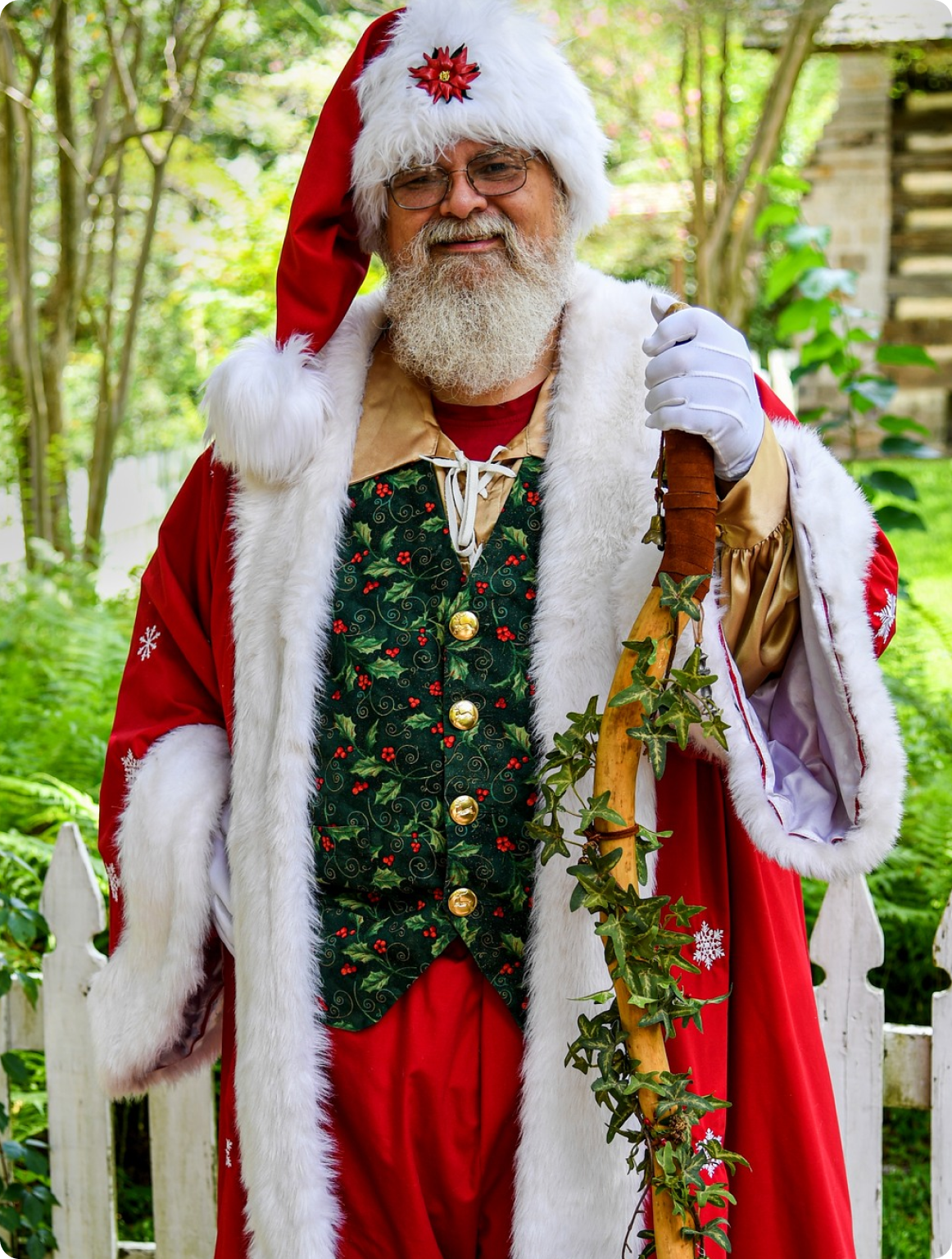 A man dressed as santa claus standing in front of trees.