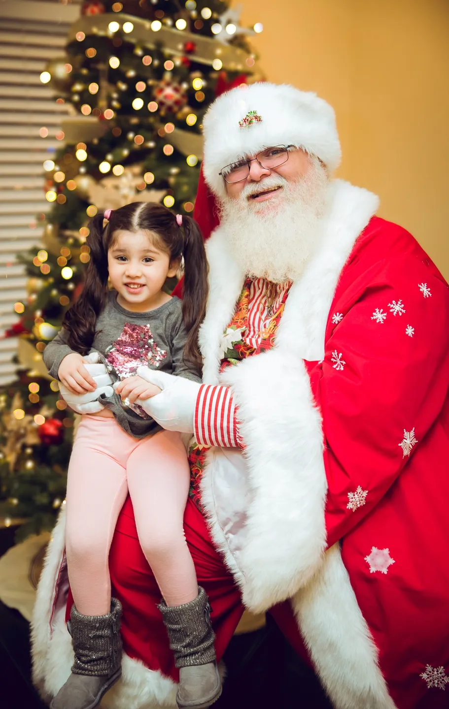 A little girl is holding a video game controller while sitting on santa 's lap.