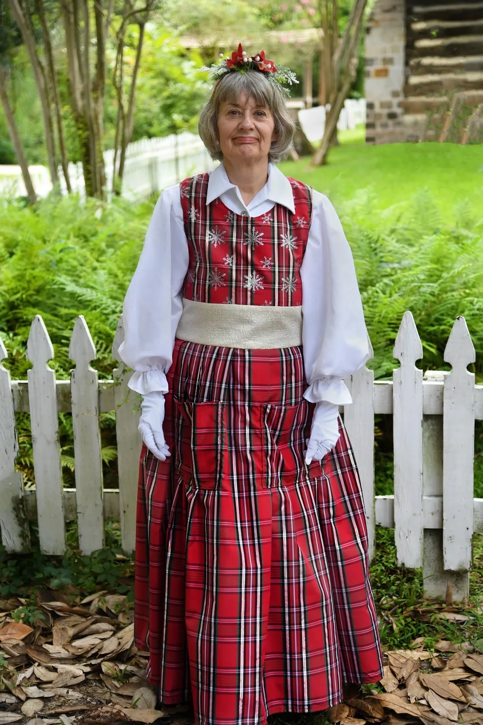 A woman in red plaid dress standing next to white fence.