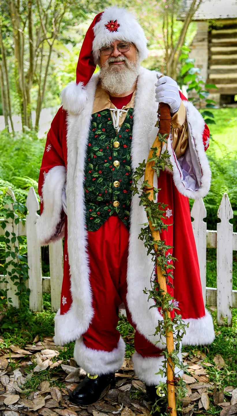 A man in santa clause costume standing next to fence.