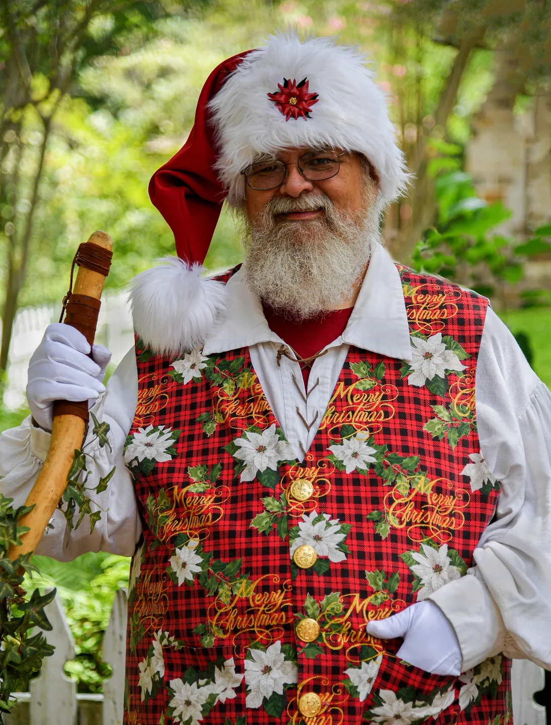 A man in a santa hat and vest holding a wooden stick.